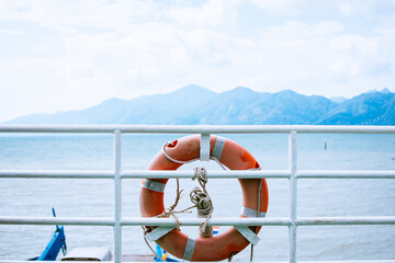Rubber ring on the ship with backdrop of the sea landscape. Orange lifebuoy on the ferry's deck.
