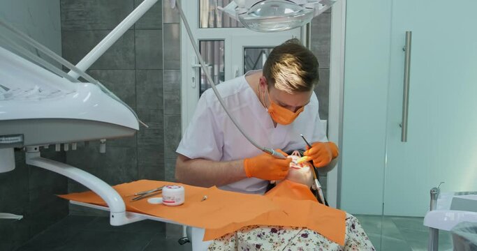 specialist dentist male in gloves and mask makes professional hygiene procedure for teeth of patient who with dilator in mouth lies in stomatology chair in clinic