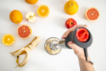 Black electric hand blender and accessories with sliced fruits on a white background. Top view, flat lay
