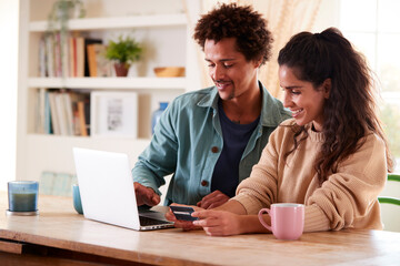 Couple With Credit Card At Home Use Laptop To Review Finances For Starting Independent Business
