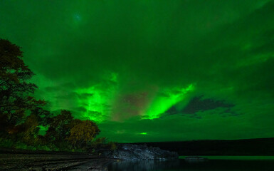 Northern lights over the plain lake and stone beach