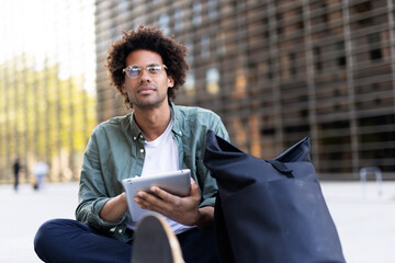 Young man with curly hair using digital tablet. Man sitting outside taking a break..