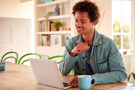 Smiling Man At Home With Laptop Reviewing Finances For Starting Independent Business