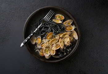 Squid ink spaghetti vongole with clams in black plate. Seafood pasta with mussels over texture background. Mediterranean delicacy food on dark rusty table copy space, top view, flat lay