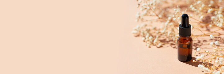 Amber bottle with dropper pipette with serum or essential oil. Beige background with daylight with beautiful flowers and shadows. Skincare natural cosmetic. Beauty concept for face and body care