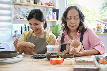 Relaxed asian aged woman and young woman concentrated painting their handmade ceramic cup