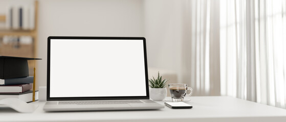 Minimal white bright home workspace with notebook laptop and graduation cap.