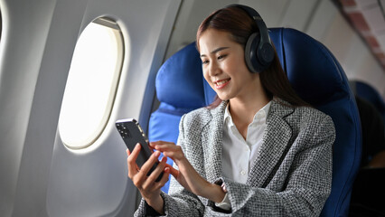 Successful businesswoman using smartphone, listening to music on headphones during the flight