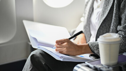 Professional businesswoman writing something on a document, remote working on the plane.