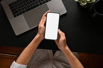 A man's hands holding a smartphone mockup over modern black workspace