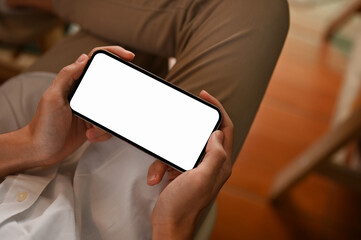 Close-up, A young man sitting on the chair, using smartphone. Phone white screen mockup.