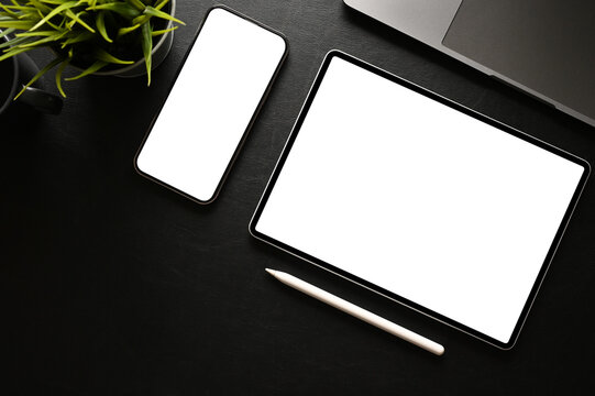 Modern black office desk workspace top view with smartphone and tablet white screen mockup