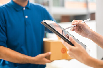 Hand woman signing electronic Signature on tablet for agreement of contract digital receiving parcel from blue delivery man from shopping online. Courier man delivering package to destination.