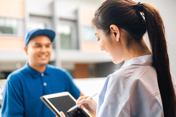 Young woman signing electronic Signature on tablet for agreement of contract digital receiving parcel from blue delivery man from shopping online. Courier man delivering package to destination.