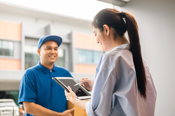 Young woman signing electronic Signature on tablet for agreement of contract digital receiving parcel from blue delivery man from shopping online. Courier man delivering package to destination.