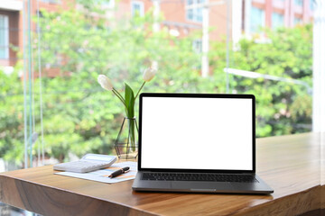 Mockup laptop computer with white empty screen on wooden table near large office window