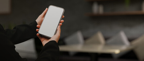 A female hands holding a mobile phone white screen mockup over blurred modern living room