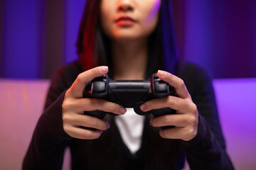 Close up hands Playing video game. Young pretty woman sitting on sofa holding joystick in living room. Female Professional Streamer  wearing hoodie playing game online in dark room neon light.