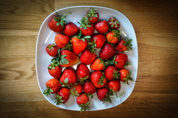 Strawberries on plate, wooden table - top view