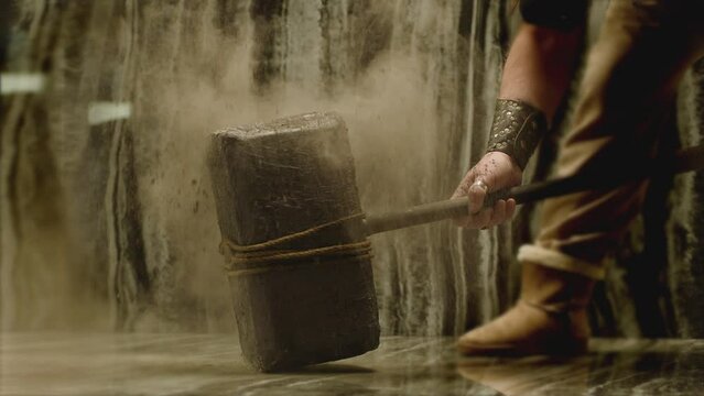 Old stone age large hammer hitting floor and spraying dust . Viking man hitting floor with huge sledgehammer. Strength and durability concept . Shot on ARRI Alexa cinema camera in 200fps Slow motion