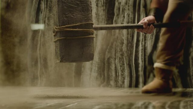 Old stone age large hammer hitting floor and spraying dust . Viking man hitting floor with huge sledgehammer. Strength and durability concept . Shot on ARRI Alexa cinema camera in 200fps Slow motion