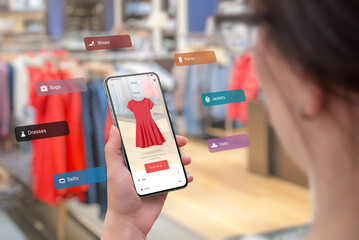Shopping with smart phone and augmented reality app in the boutique concept. Trying on the latest clothes of different sizes and colors. Woman holding smart phone - obrazy, fototapety, plakaty