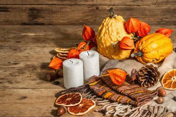 Autumn cozy composition. Scarf, warm mittens, candles, pumpkins, fall decor. Wooden background