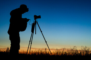 Silhouette of the photographer with tripod. Young man taking photo with his camera during golden hour.