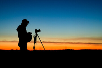 Silhouette of the photographer with tripod. Young man taking photo with his camera during golden...