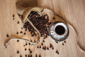 Roasted coffee beans in little bag with ropes and cup of coffee with drink on dark brown wooden...
