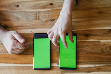 Two mobile devices with chroma screen on a wooden table. Hands using technology.