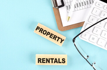 Property Rentals text written on wooden block with clipboard,eye glasses and calculator Business concept.