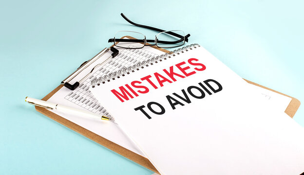 MISTAKES TO AVOID text on notepad on clipboard with chart on blue background, concept closeup. Business and finance concept