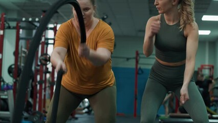 Woman with overweight exercising with battle ropes and female trainer at the gym. Shot with RED helium camera in 4K.  