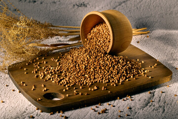 Buckwheat in an overturned wooden cup on a wooden board with dry flowers in the background