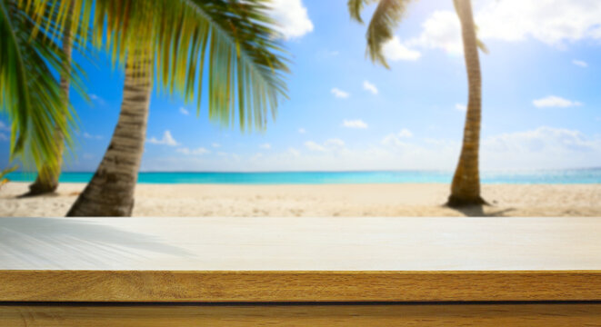 Empty wooden table over blurred sunny tropical beach background. Outdoor party mock up for design and product display.
