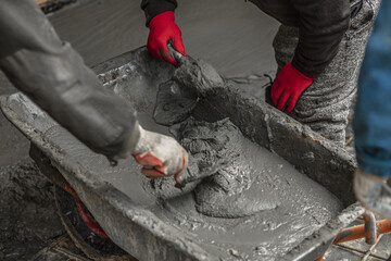 Men kneads cement mortar in an iron wheelbarrow, male hand with trowel. Concreting works, building worker. High quality photo