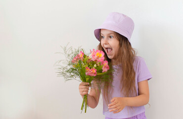 Portrait of a charming girl in a summer purple hat holding a bouquet of summer flowers and posing for the camera on a white background