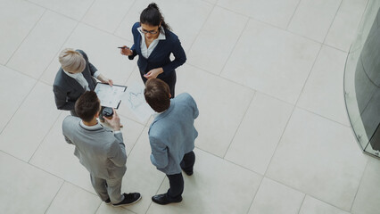 Top view of group of business people in suits discussing financial graphs in lobby of business...