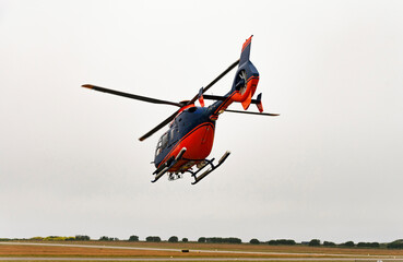 Fototapeta na wymiar Cornwall, England, UK. 2022. A modern helicopter in flight with covered tail rotor and painted red and blue colours.