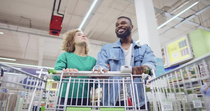 Time -apse of multiethnic couple with shopping cart walking in diy store. Realtime