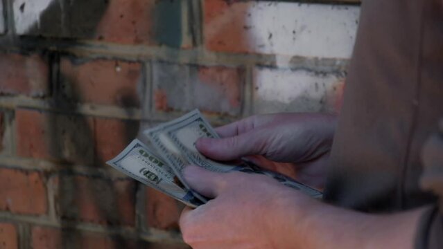 close up man is counting money for drugs, standing against brick wall in remote alley. criminal business. slow motion. drug trafficking concept.
