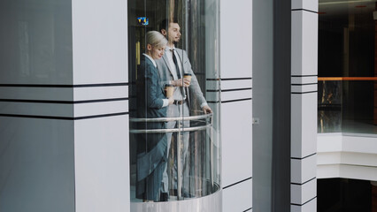 businesswoman and businessman colleagues talking in moving elevator in modern business center...