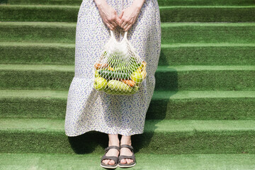 Knitted mesh bag with vegetables and fruits in the hands of a woman. Zero waste grocery shopping...