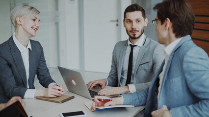 Obraz premium Businessman discussing future business project with male and female colleagues sitting at the table in modern office indoors