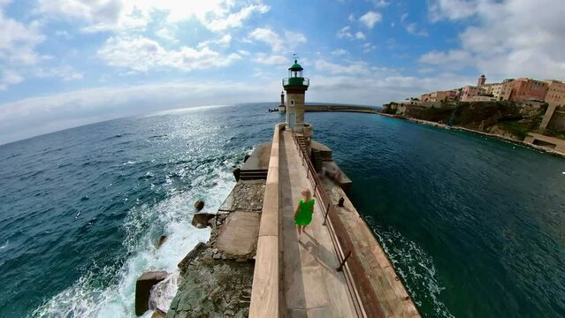 Top view of a tourist woman walking on the pier of the harbor of Bastia city to the lighthouse. In Corsica island of France. Aerial view of cityscape with the lighthouse of the city port in Tyrrhenian