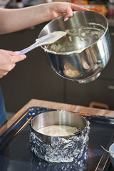 female hands shift the batter from an iron bowl with a spatula into a round iron baking dish