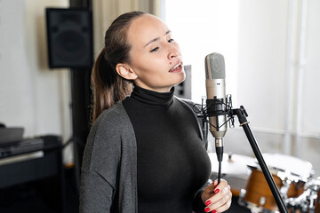 Young Asian or Caucasian brunette woman singing lyric song to microphone alone in professional...