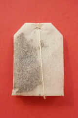 One white tea bag on red table, top view