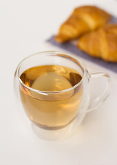 Herbal tea in a glass cup on a white table and two croissants on a towel against the background